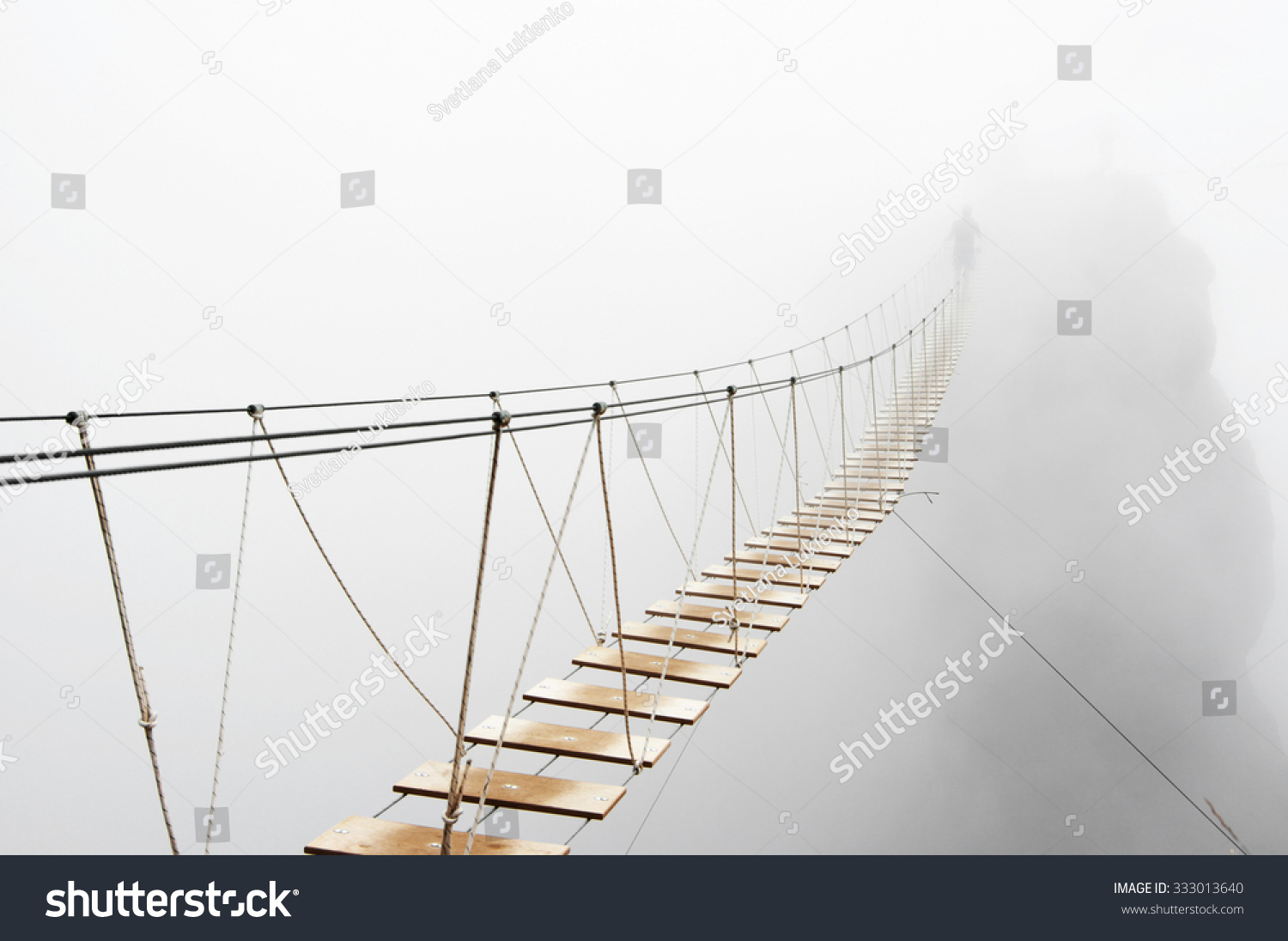 Fuzzy man walking on hanging bridge vanishing in fog. Focus on middle of bridge.  #333013640