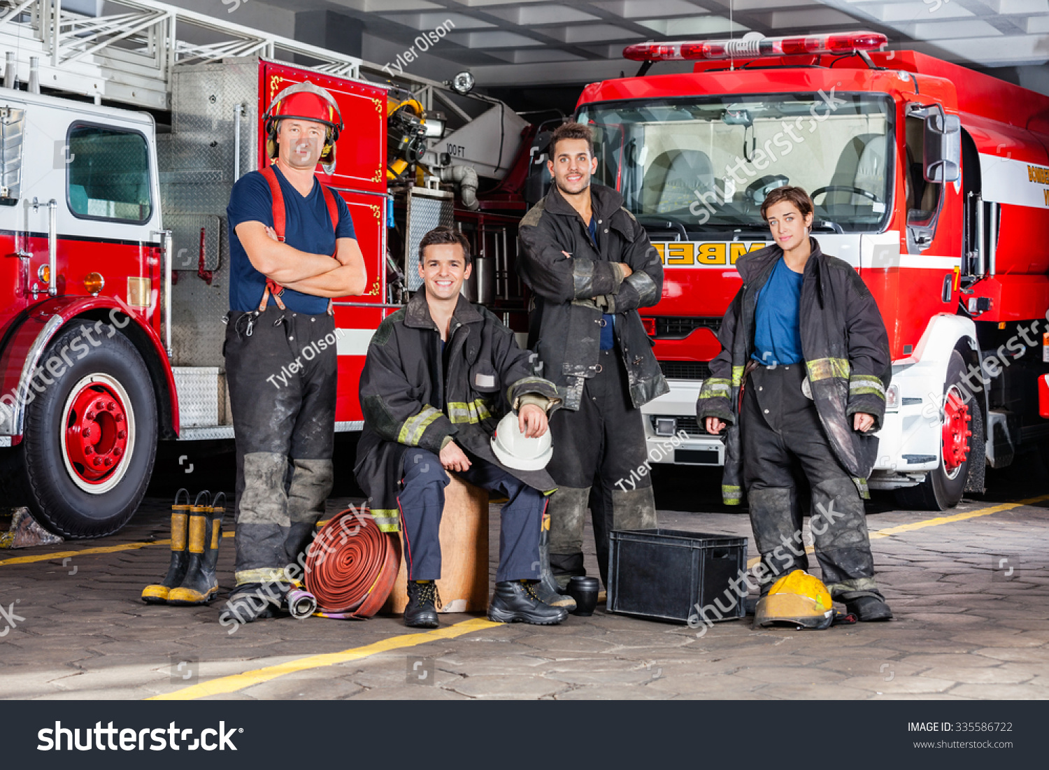 Portrait of confident firefighters with equipment against trucks at fire station #335586722