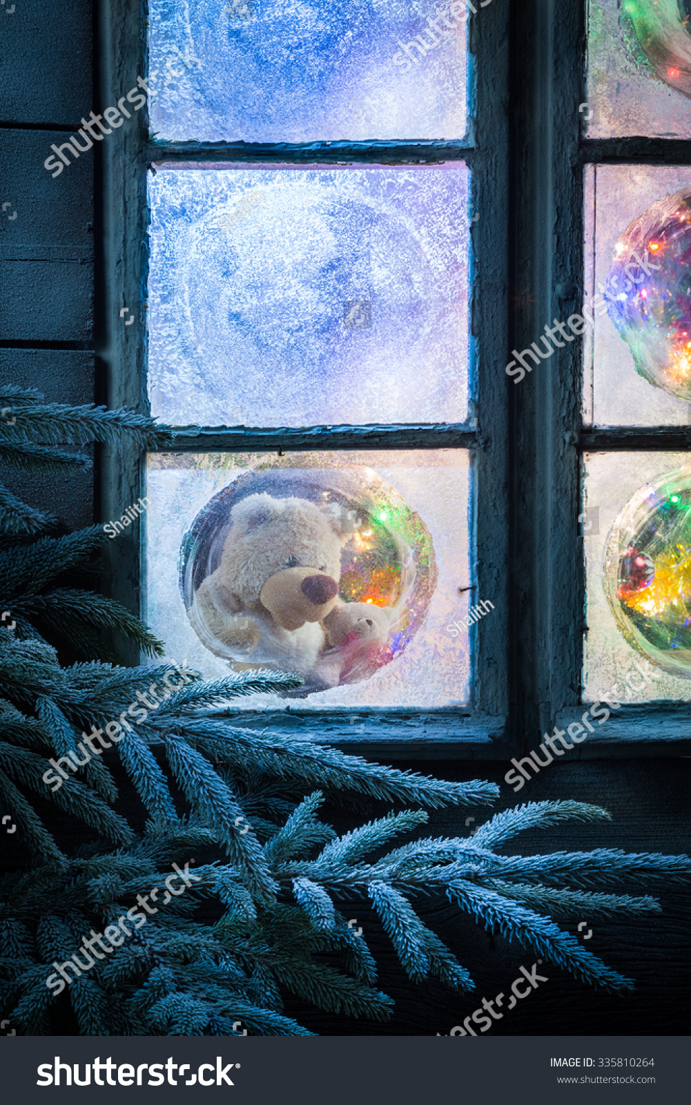 Teddy bear in frozen window for Christmas with tree and lights #335810264