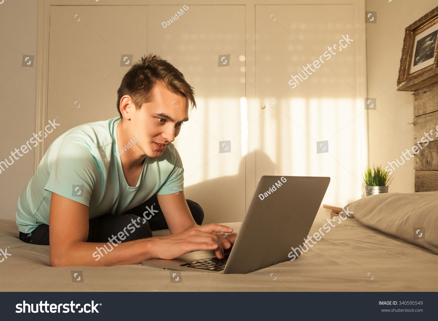 Man typing in a laptop computer while sitting in the bedroom. #340595549