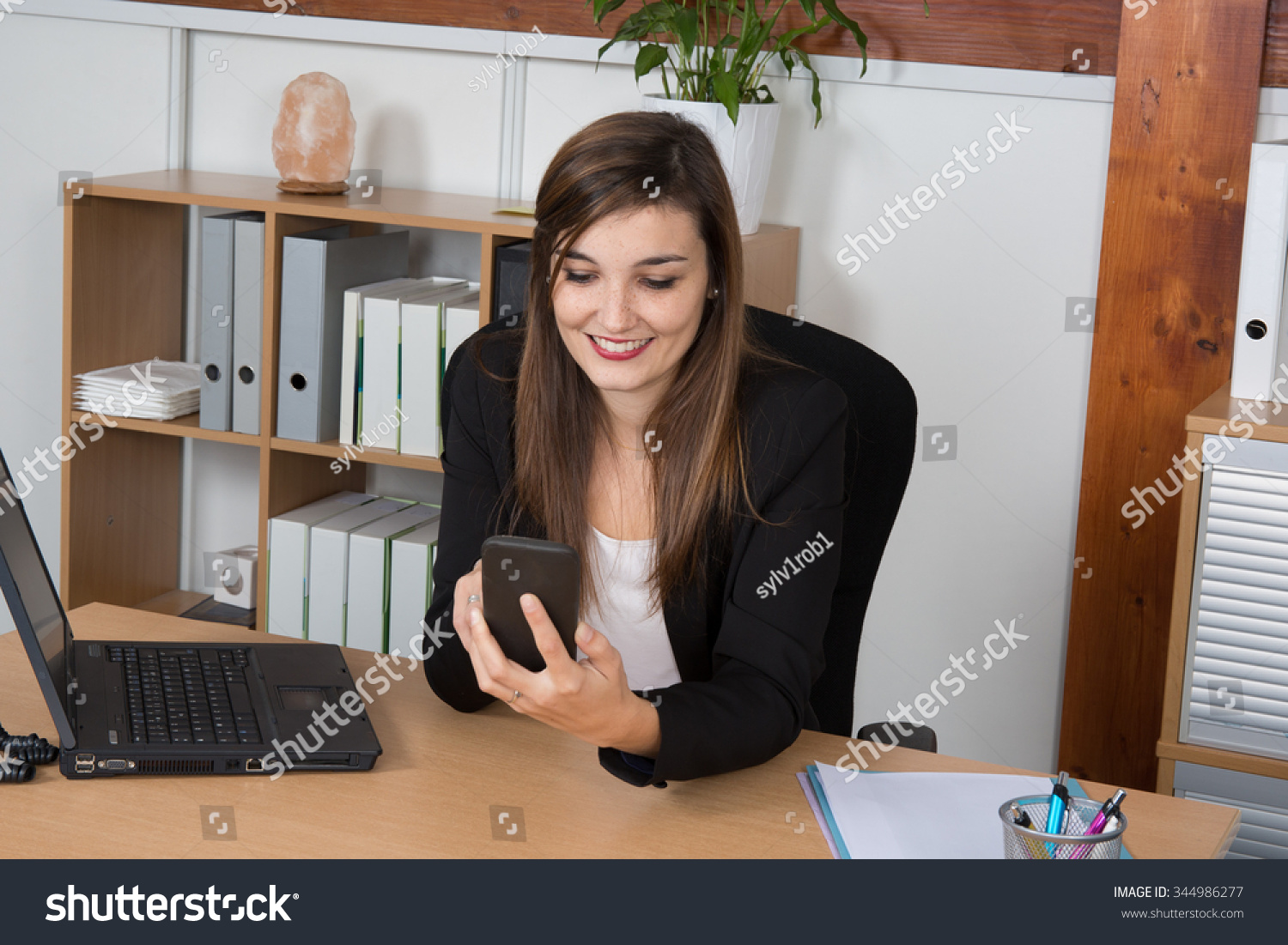 Happy office worker reading a text message at a bright office #344986277
