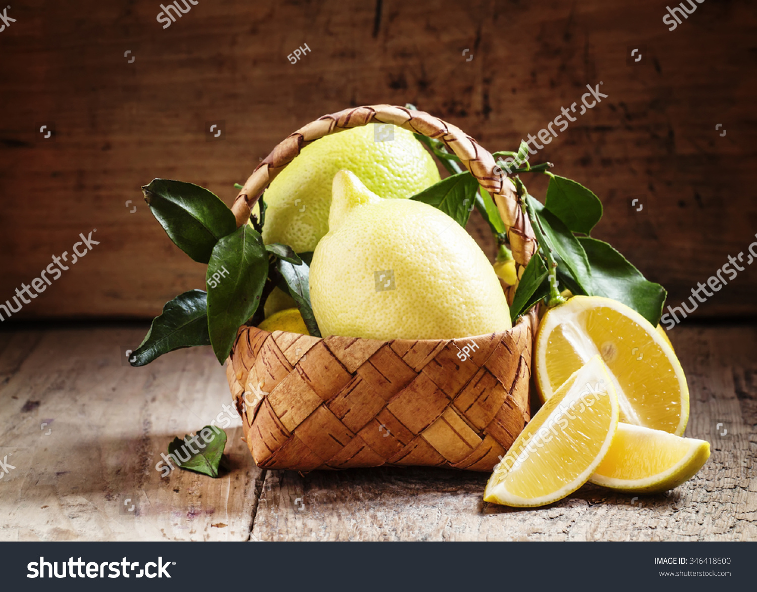 Slices of lemon and cut lemons with leaves in a wicker basket on an old wooden table in rustic style, selective focus #346418600