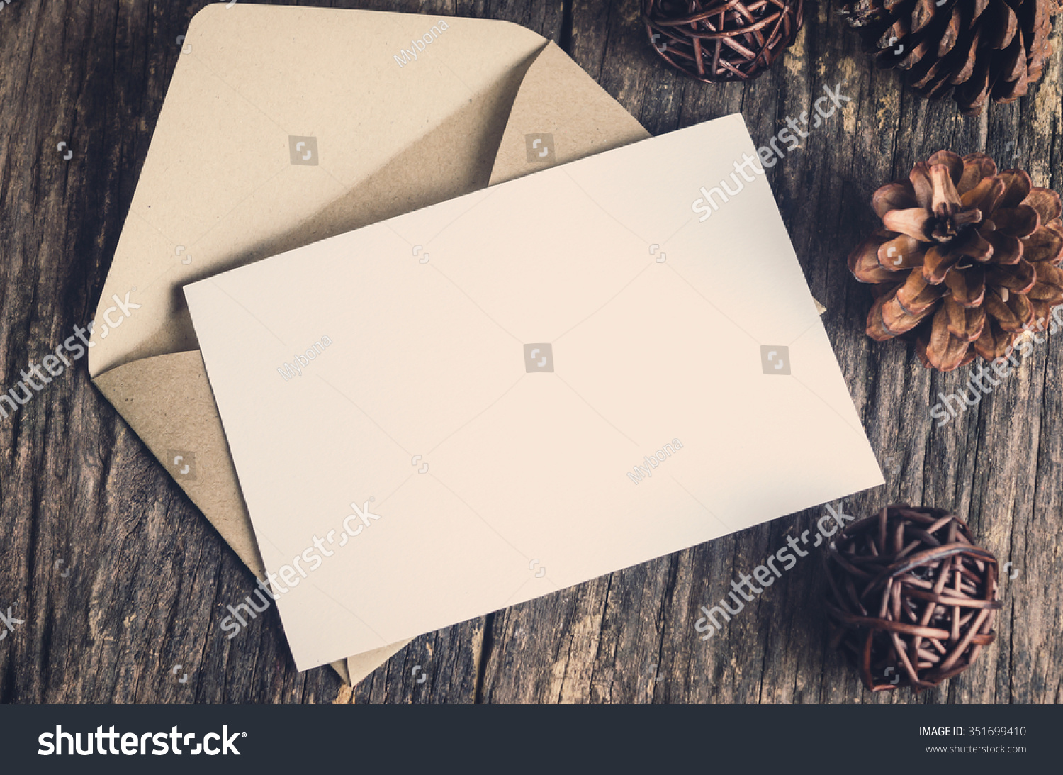 Blank white paper card with brown envelop and pine cones on old wooden table with vintage and vignette tone #351699410