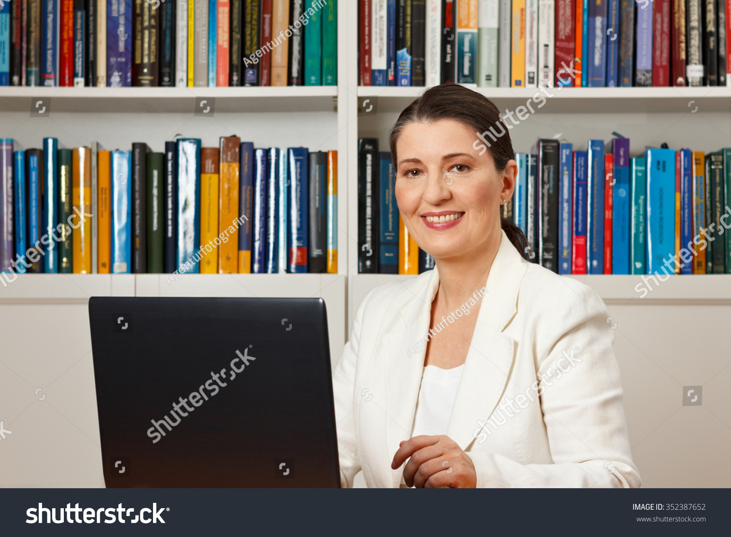 Friendly smiling woman in front of a computer in a library, consultant, counselor, adviser, customer service, online helpline #352387652