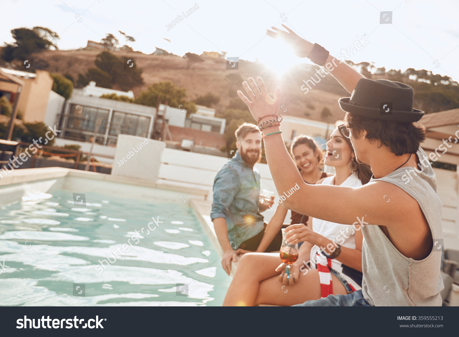 Young people sitting on the edge of the pool enjoying a party. Young woman singing during a the party. Multiracial friends having fun during rooftop party. #359555213