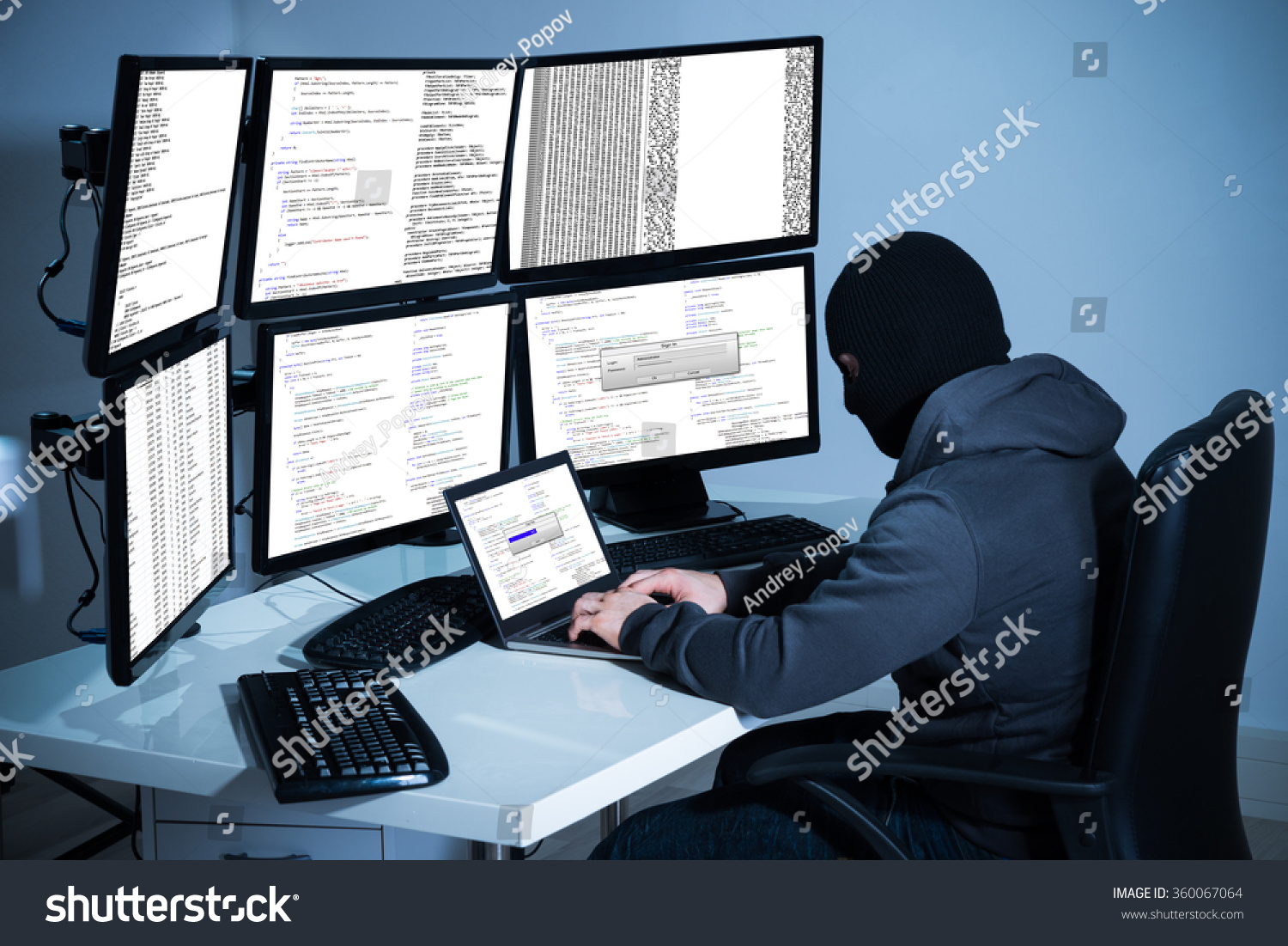 Male hacker using laptop against multiple monitors at desk in office #360067064