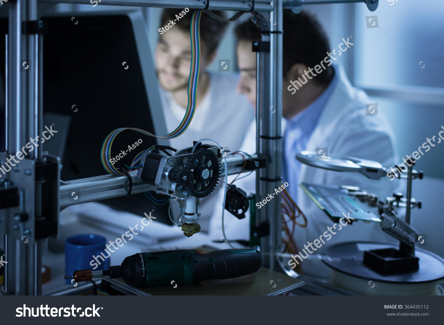 Young engineers working in the laboratory and using a computer, 3D printer on foreground, science and technology concept #364435112