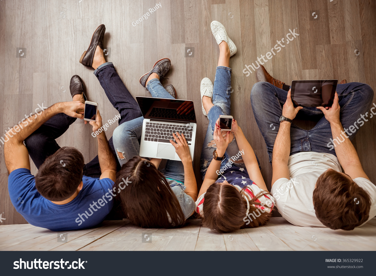 Group of attractive young people sitting on the floor using a laptop, Tablet PC, smart phones, headphones listening to music, smiling #365329922