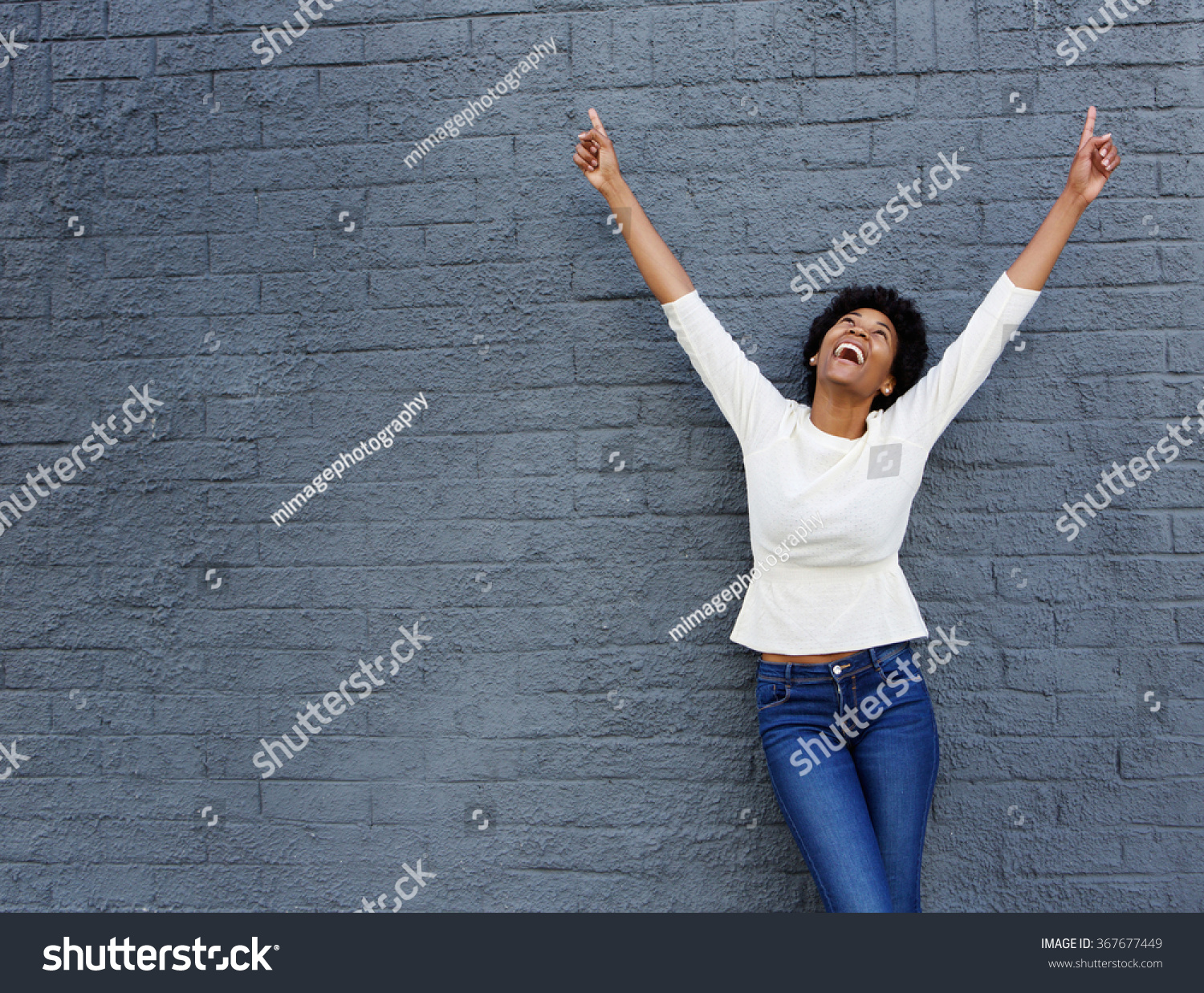 Portrait of a cheerful african woman with hands raised pointing up #367677449