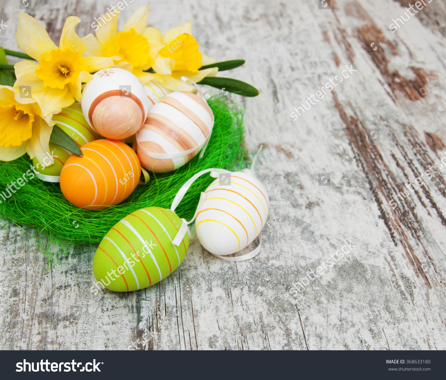 easter eggs in a nest with daffodil flowers on a old wooden background #368633180