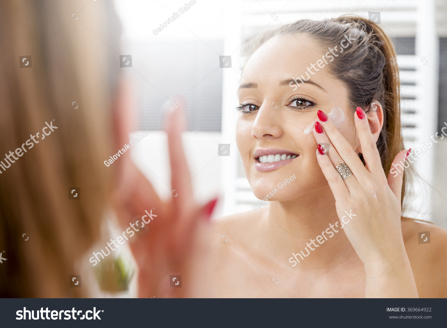 Attractive girl putting anti-aging cream on her face #369664922