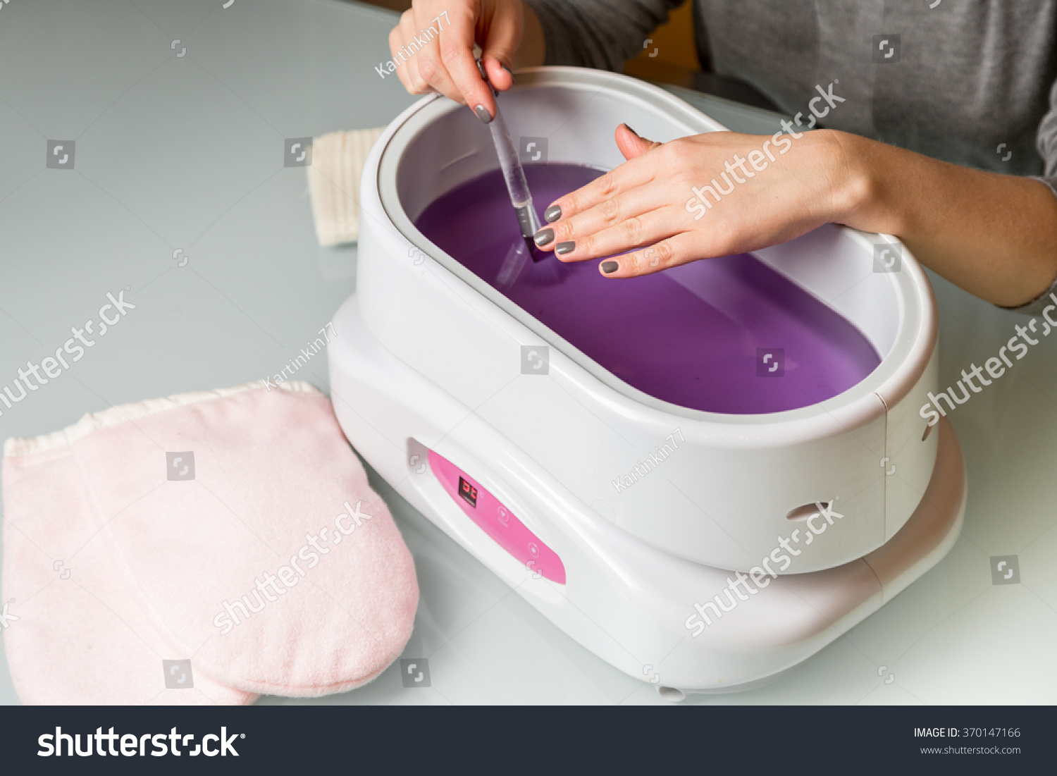Female hands taking procedure in a lilac paraffin wax  bowl. Cosmetology and skincare equipment in a beauty & spa salon. #370147166