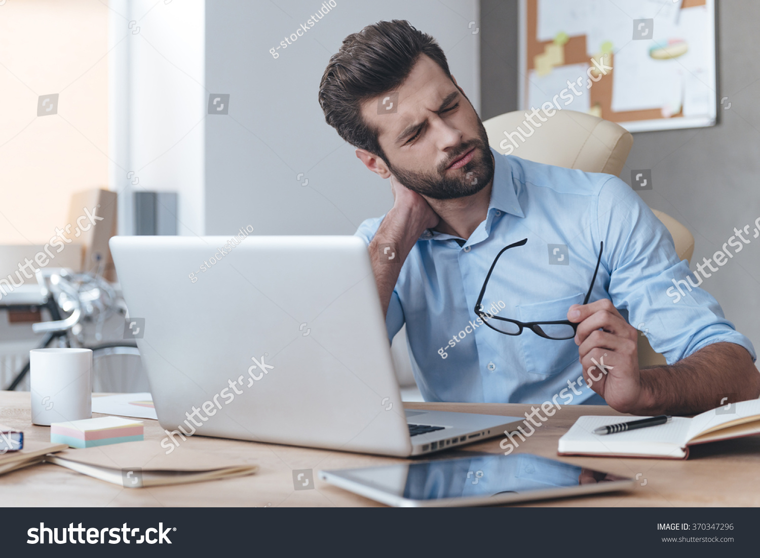 Feeling exhausted. Frustrated young handsome man looking exhausted while sitting at his working place and carrying his glasses in hand #370347296