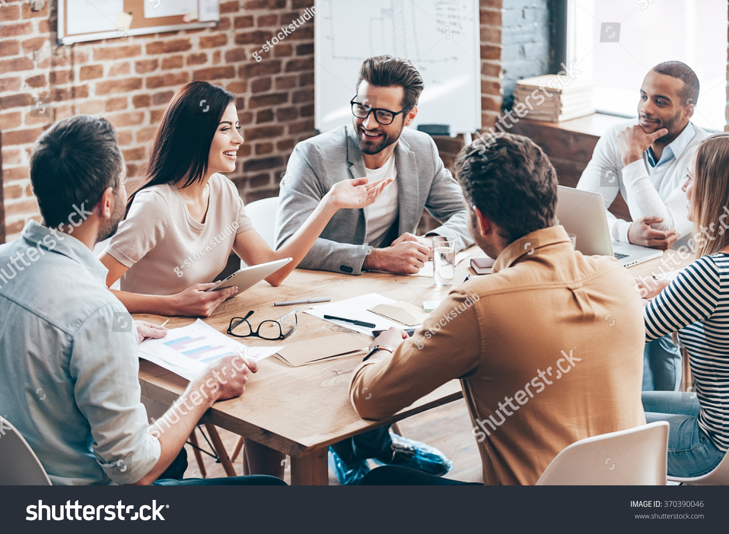 Making great decisions. Young beautiful woman gesturing and discussing something with smile while her coworkers listening to her sitting at the office table