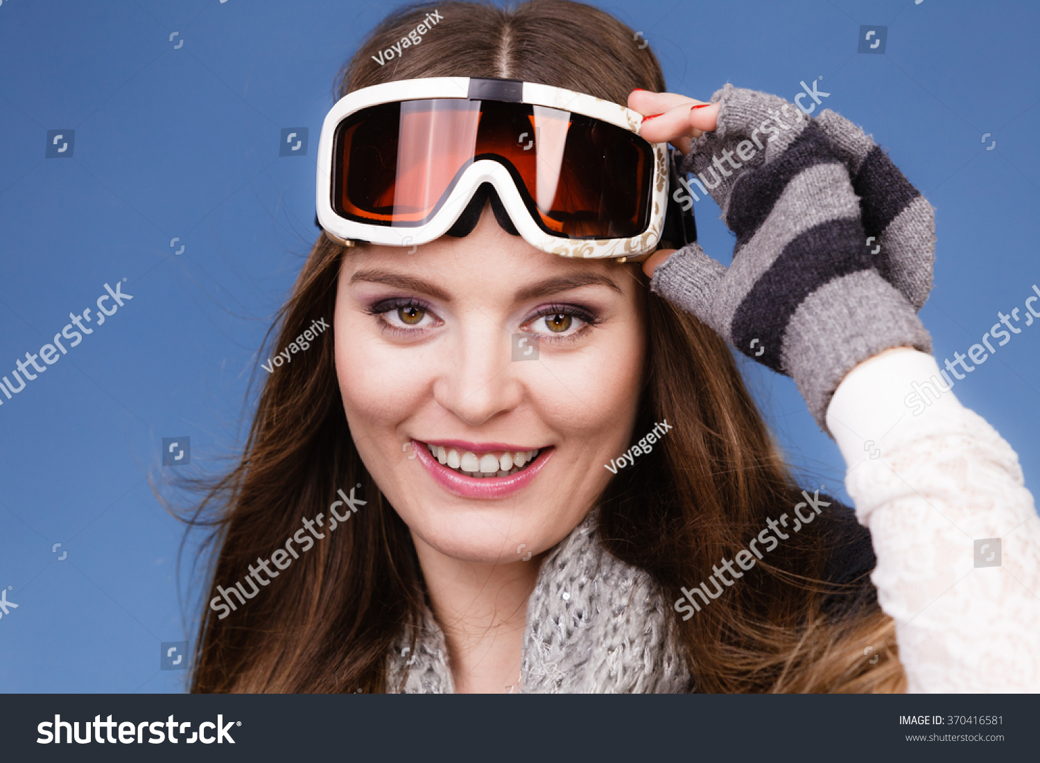 Woman skier girl wearing warm clothing ski goggles portrait. Winter sport activity. Beautiful sportswoman on blue studio shot #370416581