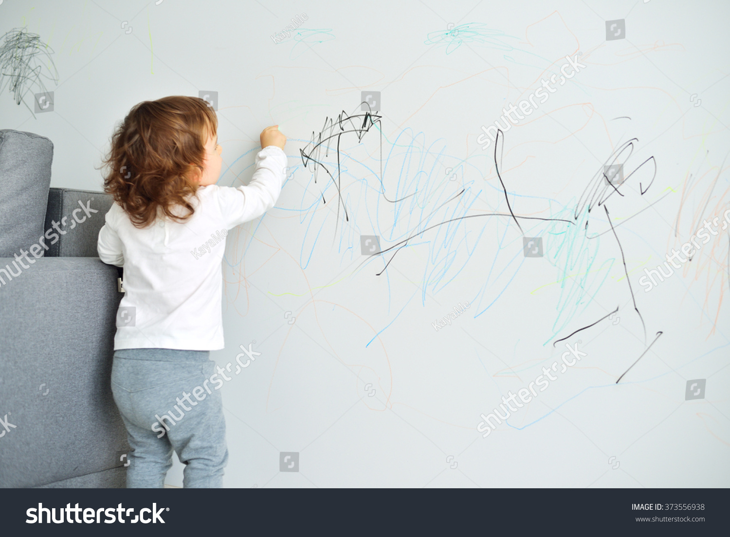 Curly cute little baby girl drawing with crayon color on the wall. Works of child #373556938