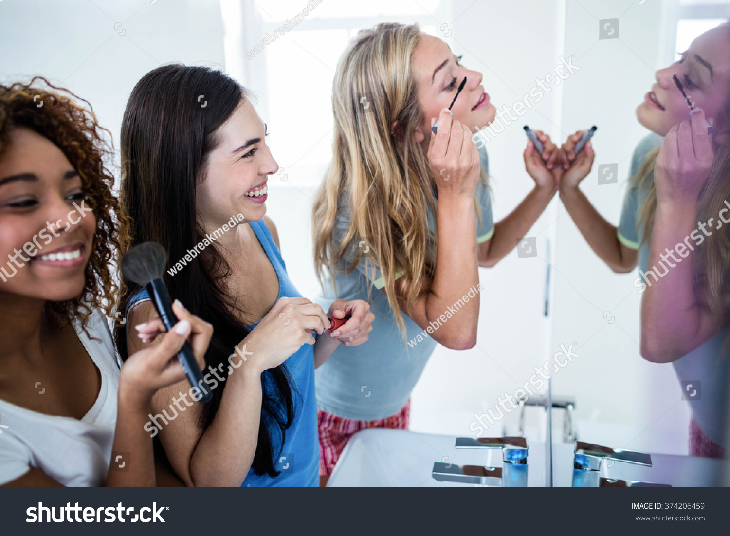 Three smiling friends putting makeup on together in the bathroom #374206459
