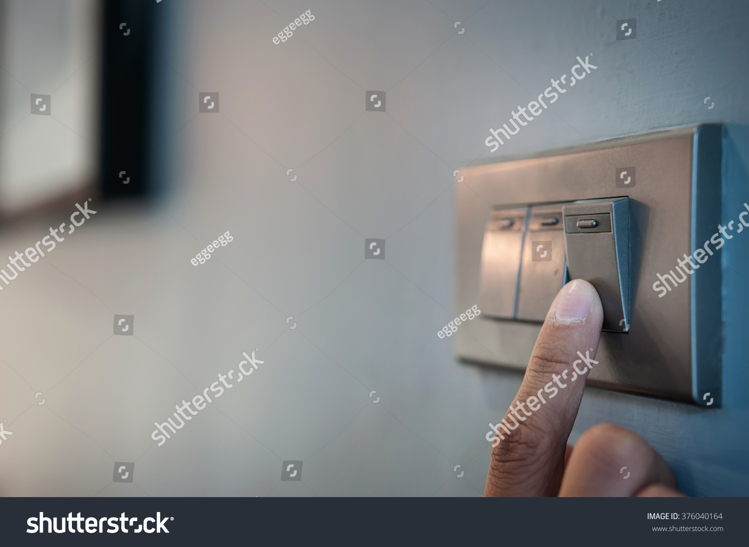 Close up male hand or fingers turn on or off on grey light switch with dark blue wall in the night time at home. Power, Energy, Safety, Saving Electrical. Copy space.  #376040164