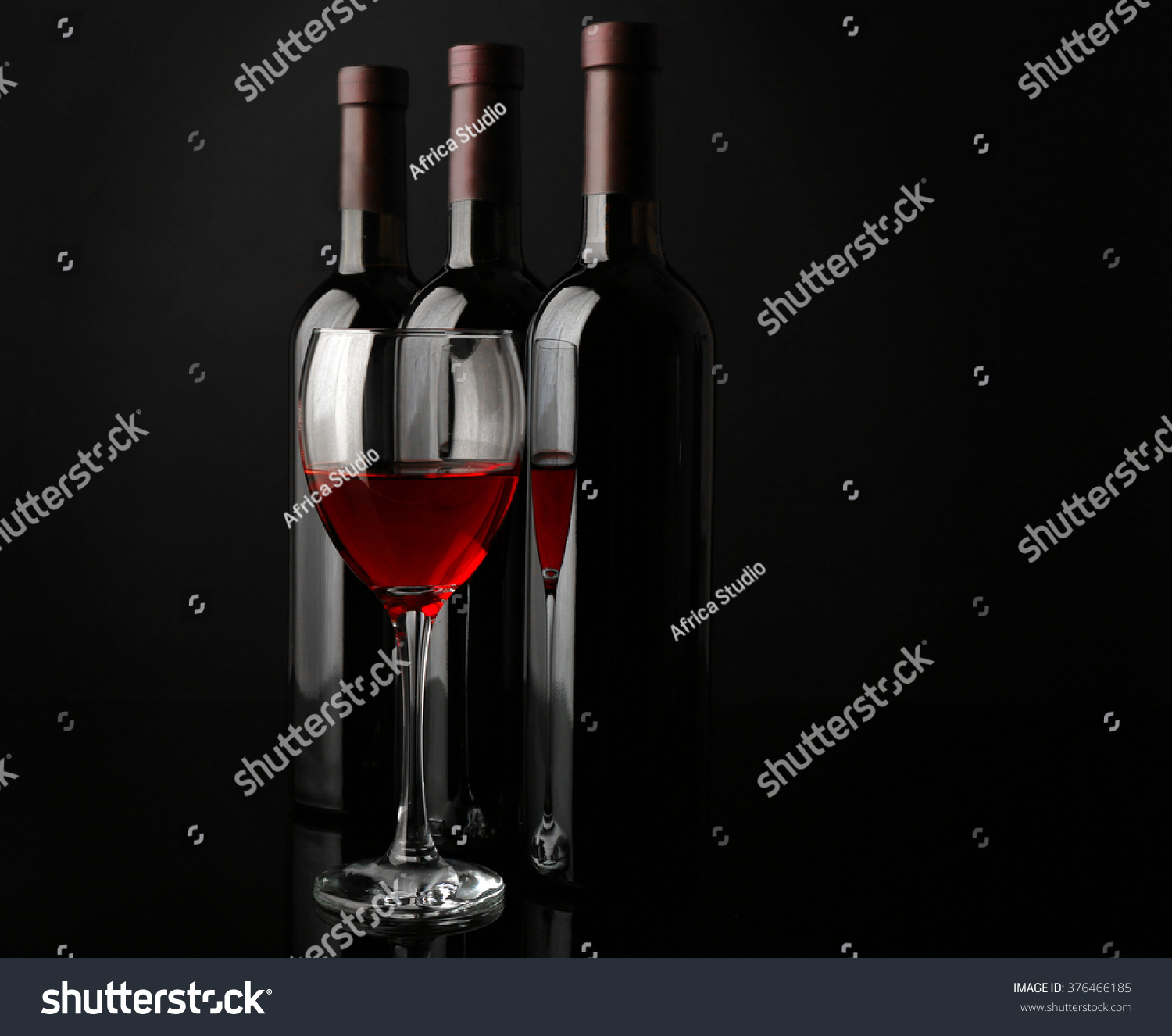 Red wine glass against bottles in a row on black background, close up #376466185