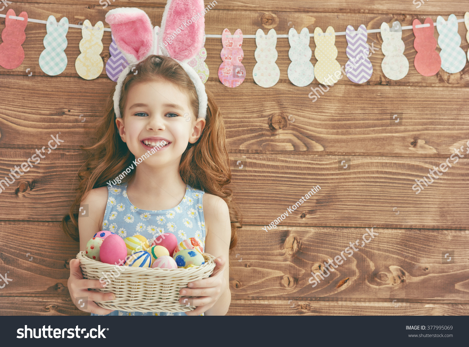 Cute little child girl wearing bunny ears on Easter day. Girl holding basket with painted eggs. #377995069