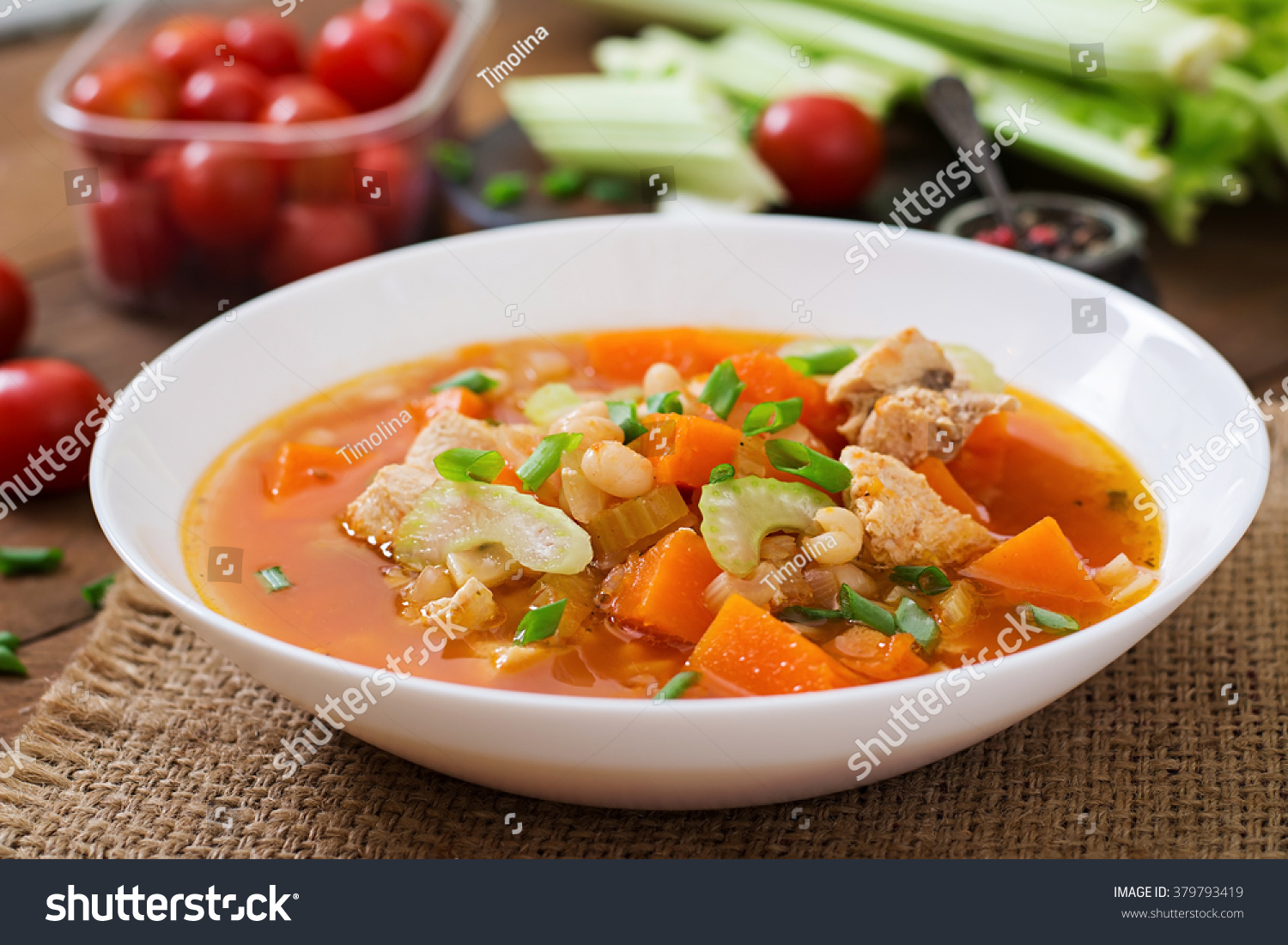 Tomato chicken soup with pumpkin, beans and celery in white bowl #379793419
