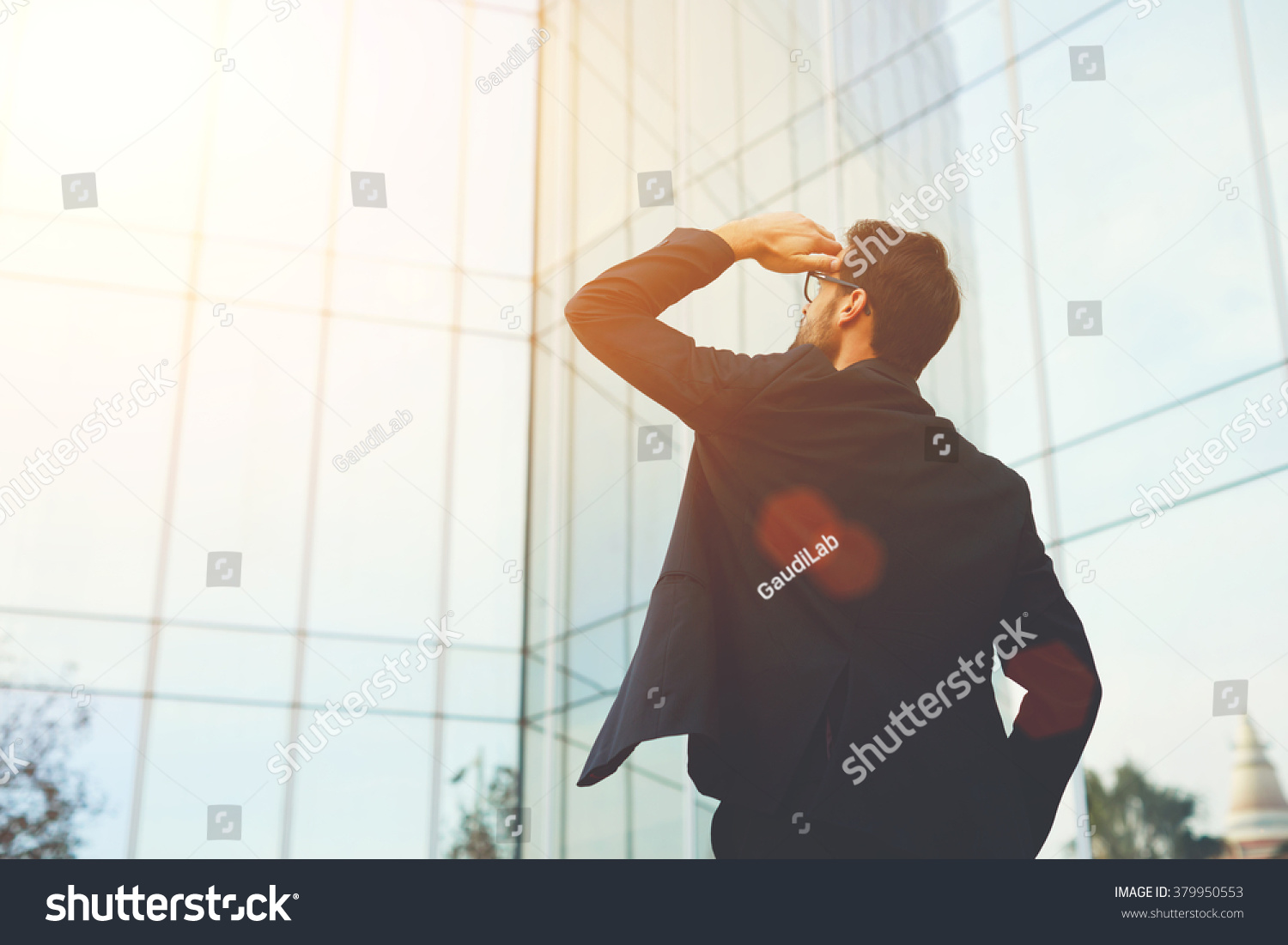 Back view of successful man entrepreneur looking up on modern skyscraper while standing outdoors, young executive male director admires something on the distance during work break outside of company #379950553