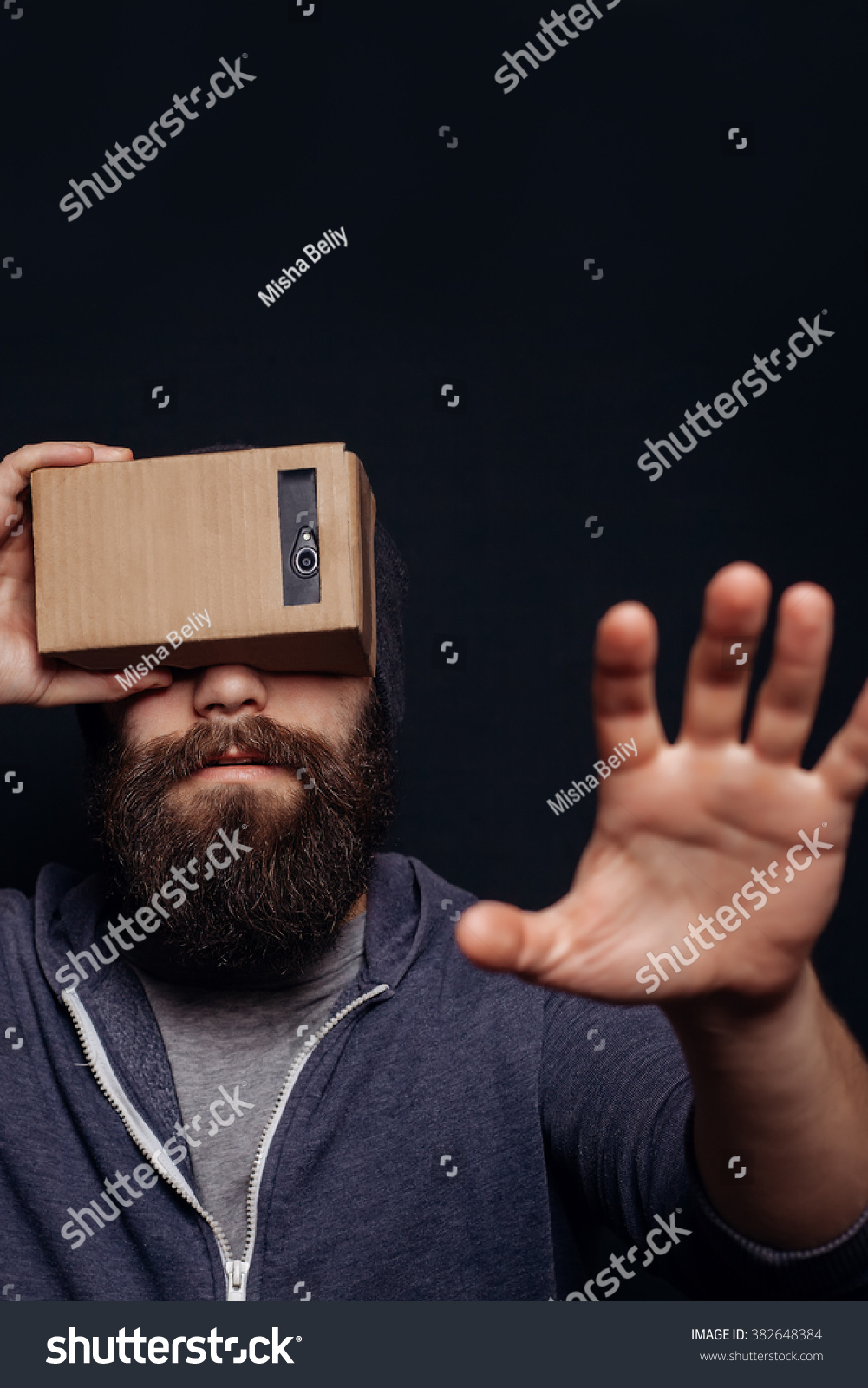 Color shot of a young man looking through a card board, a device with which one can experience virtual reality on a mobile phone. man touches the hand. blurry photos #382648384