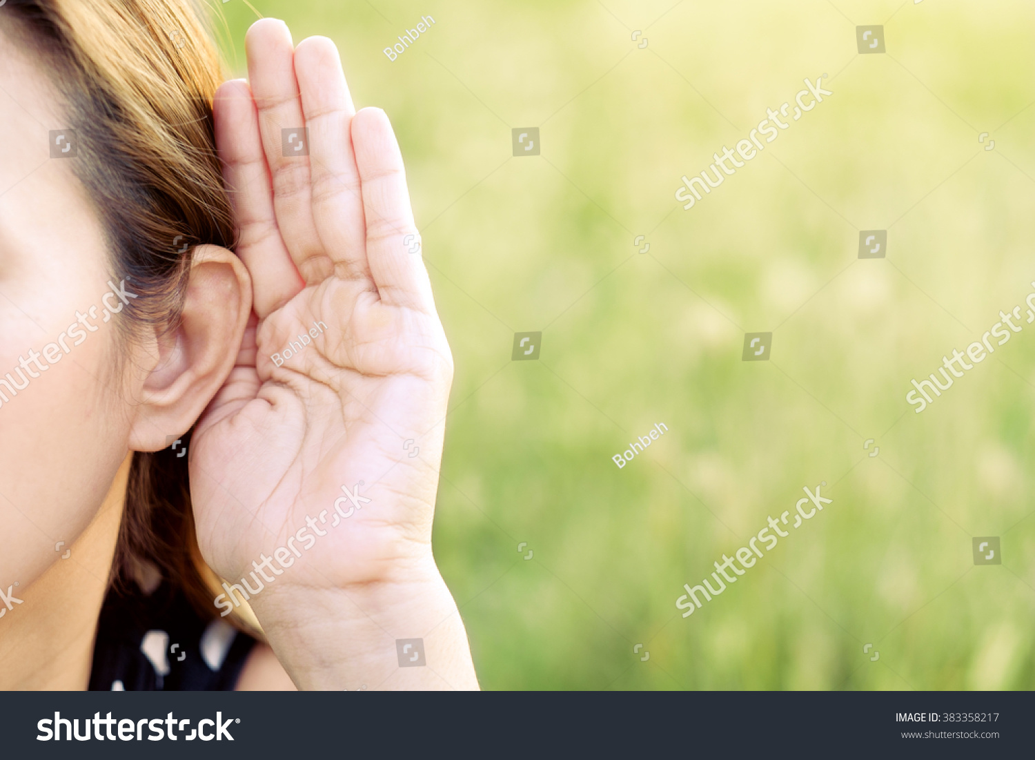 Asian woman hold her hand near her ear and listening in green field #383358217