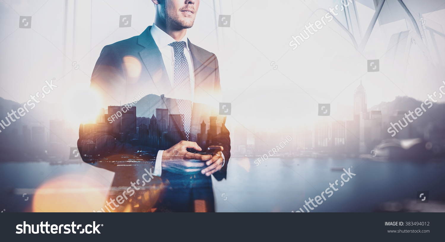Photo of businessman holding smart phone. Double exposure photo of panoramic city view at sunrise  #383494012