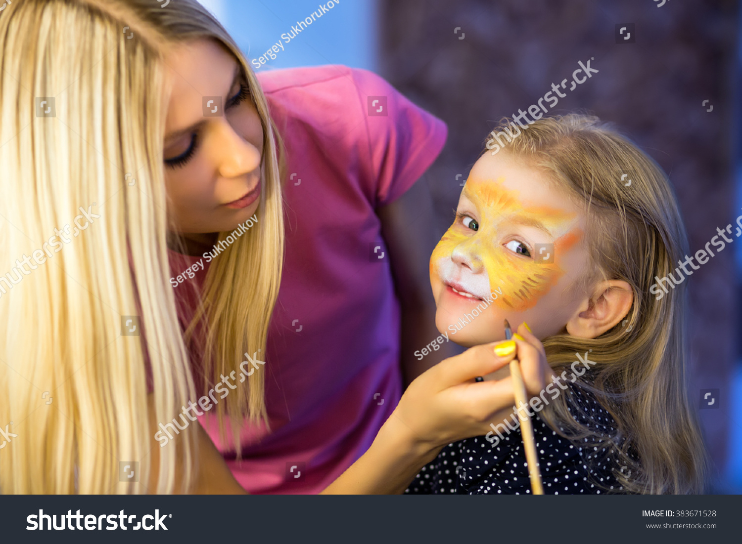 Pretty blond woman painting the face of a little girl #383671528