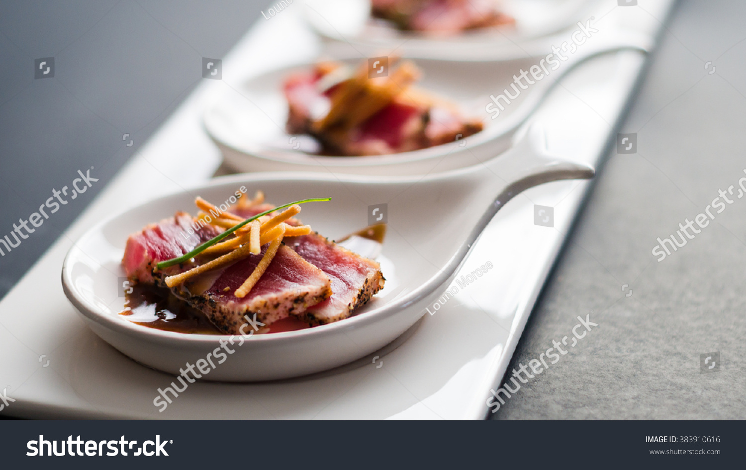 Tuna Tataki is a Japanese dish which consist of briefly seared tuna steak in thin slices. Served as appetizer with brandy sauce and garnish on a dark background. #383910616