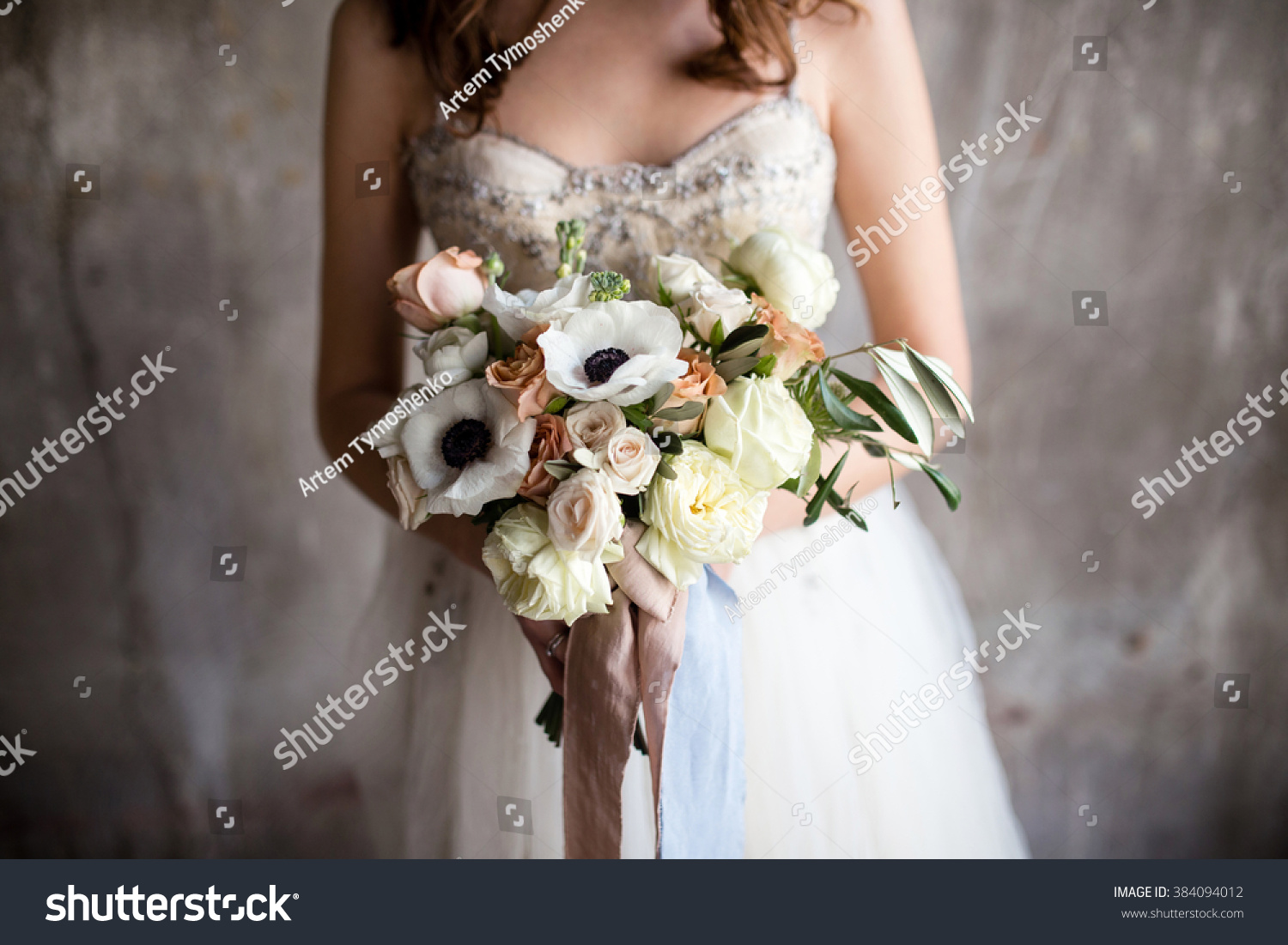 a bouquet of anemones in the hands of the bride against the background of textured walls #384094012