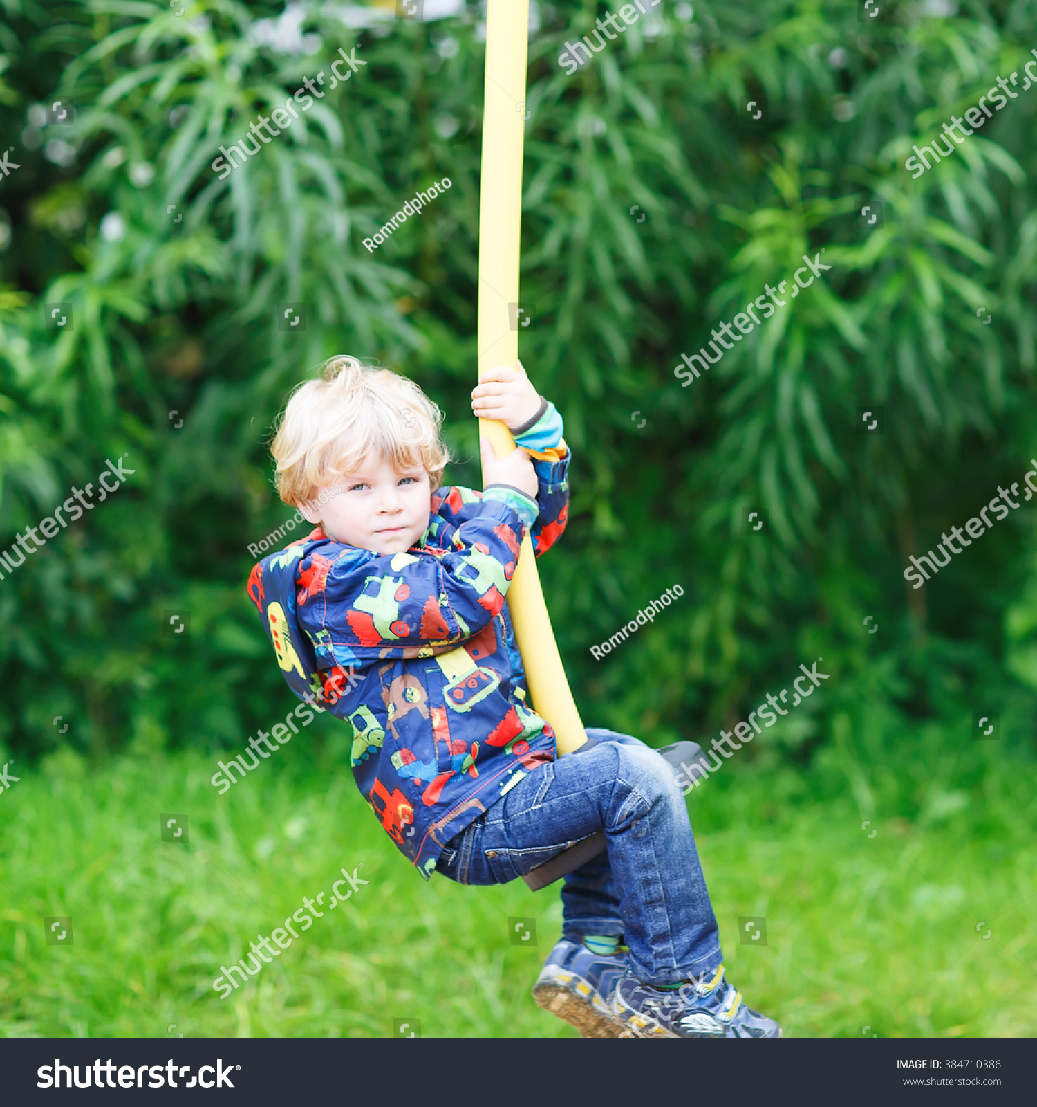 Little smiling boy of three years having fun on swing on sunny summer day, outdoors. Active sports with kids. #384710386
