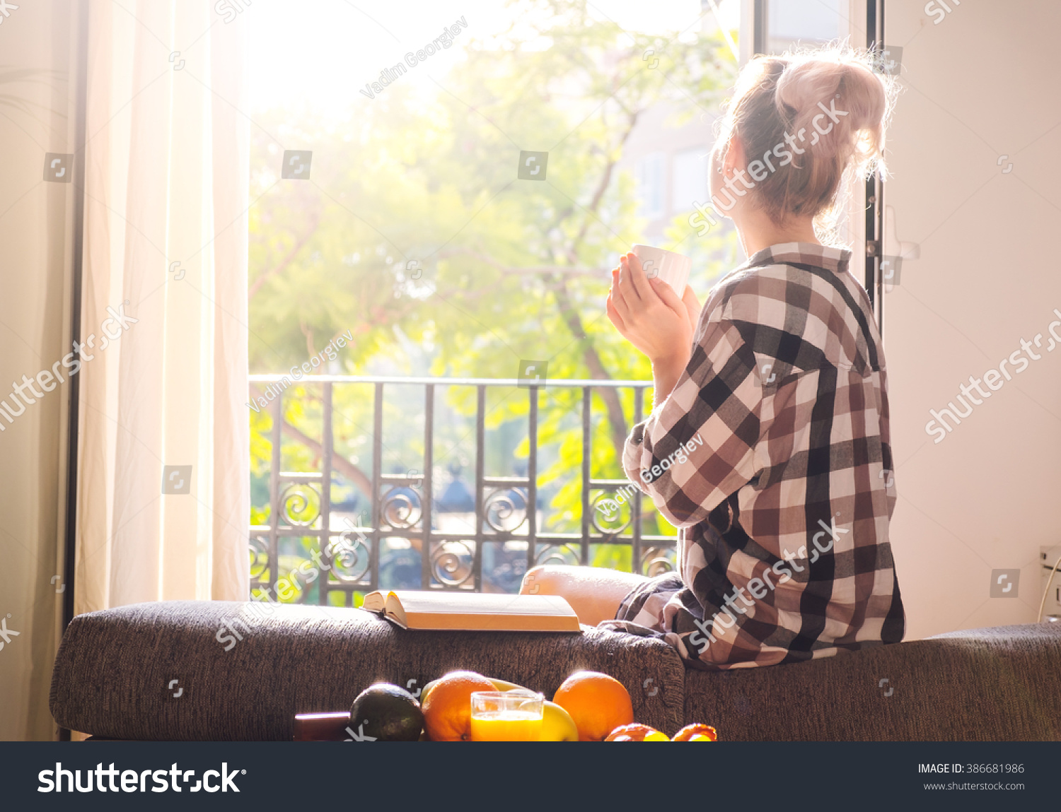 Young pretty woman  sitting at opened window drinking coffee and looking outside enjoys of rest #386681986