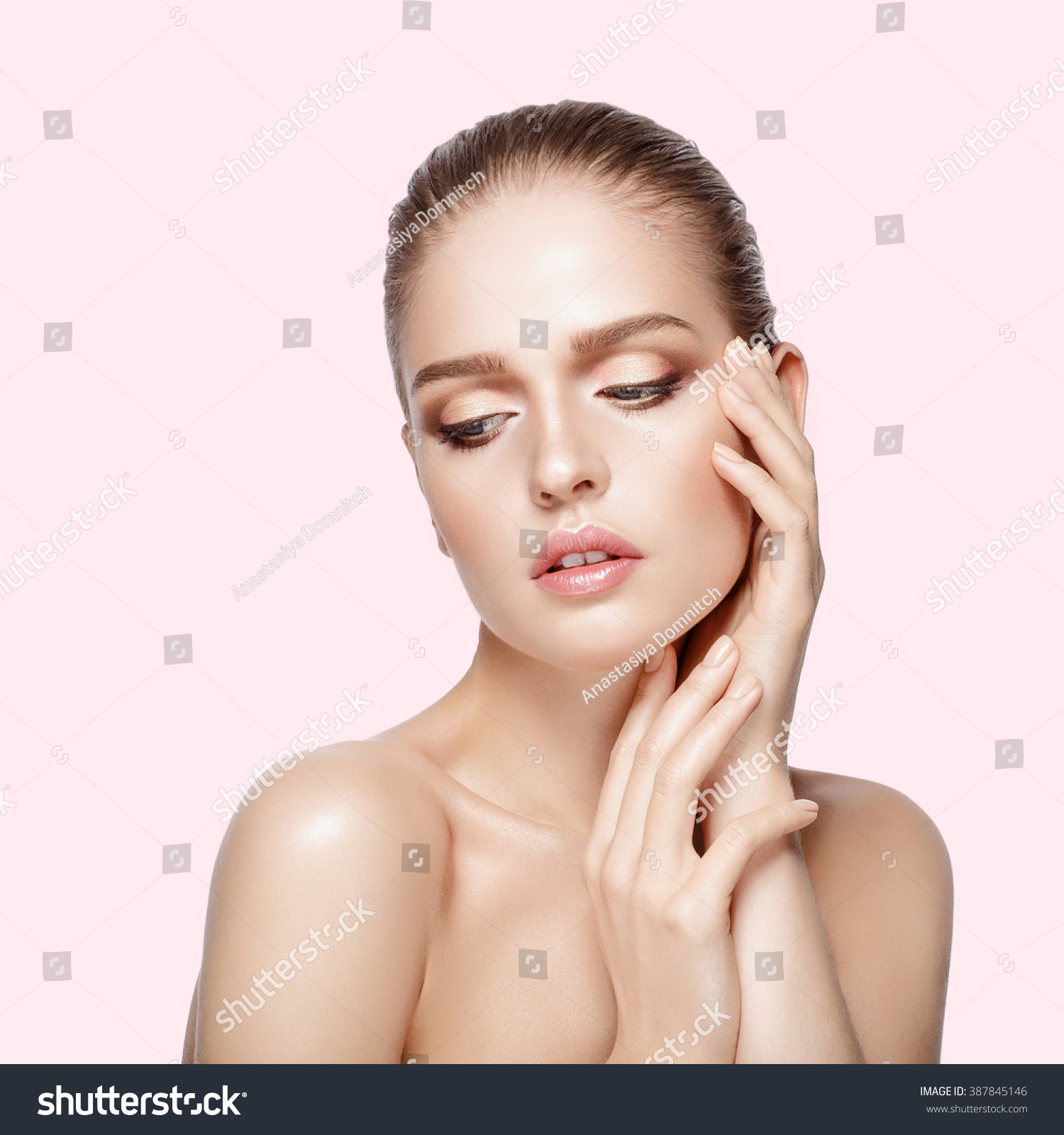 Studio portrait of young beautiful model with hands near her face on pink background. Perfect fresh clean skin. professional makeup. Brunette hair. Hands touching her face. Not isolated #387845146