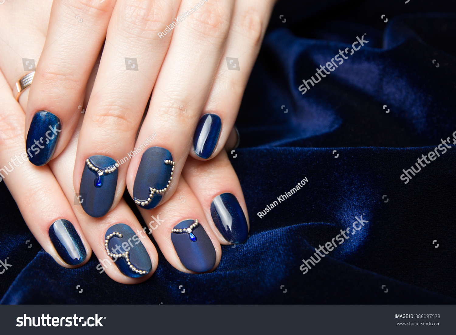 French manicure - beautiful manicured female hands with blue manicure with rhinestones on dark blue background #388097578