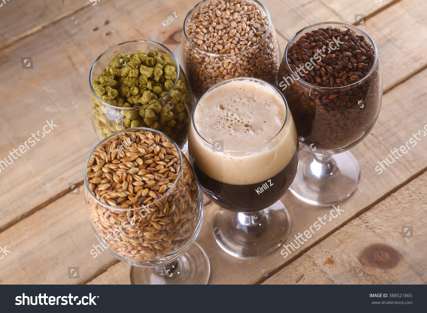 Glasses filled with dark beer, different malts and hops over a wooden background #388521865