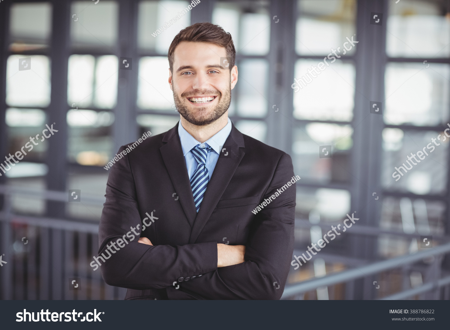 Portrait of happy businessman with arms crossed standing in office #388786822