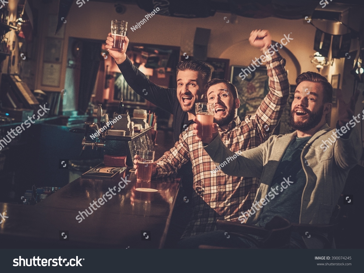 Cheerful old friends having fun watching a football game on TV and drinking draft beer at bar counter in pub. #390074245