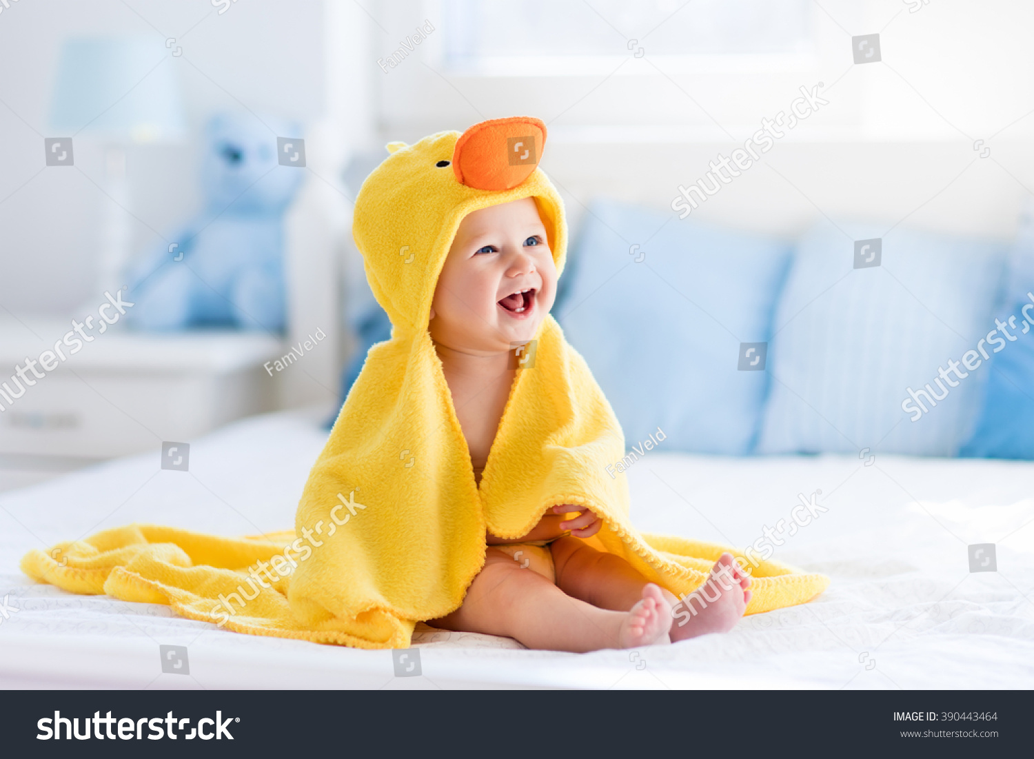 Happy laughing baby wearing yellow hooded duck towel sitting on parents bed after bath or shower. Clean dry child in bedroom. Bathing and washing of little kids. Children hygiene. Textile for infants. #390443464