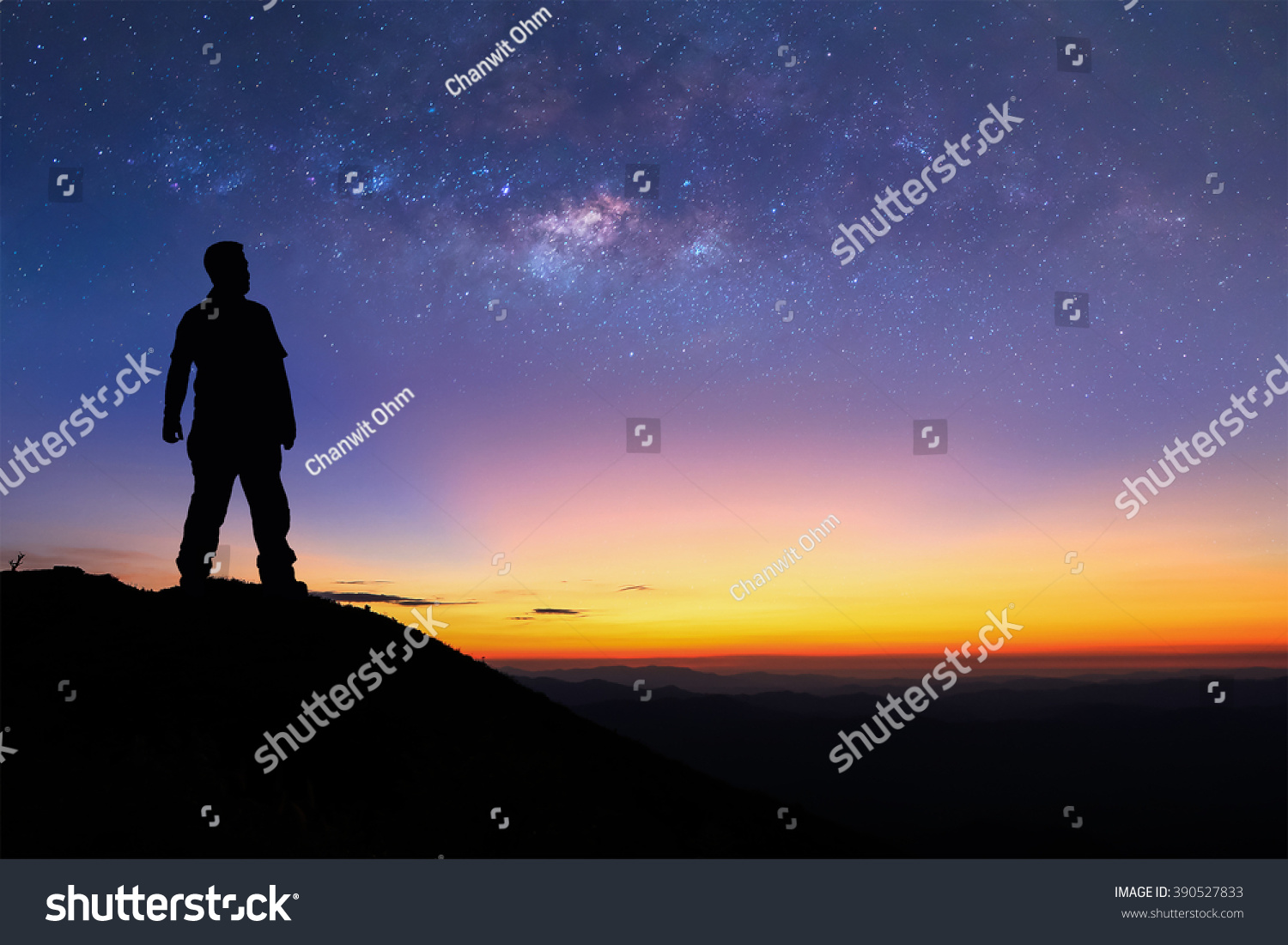 Silhouette of man is standing on top of mountain and enjoy to see the milky way before sunrise. Young tourist stand on the hill with colorful night sky on background. #390527833