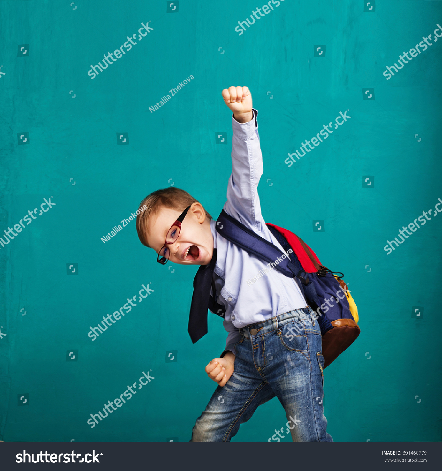 Cheerful smiling little boy with big backpack jumping and having fun against blue wall. Looking at camera. School concept. Back to School #391460779