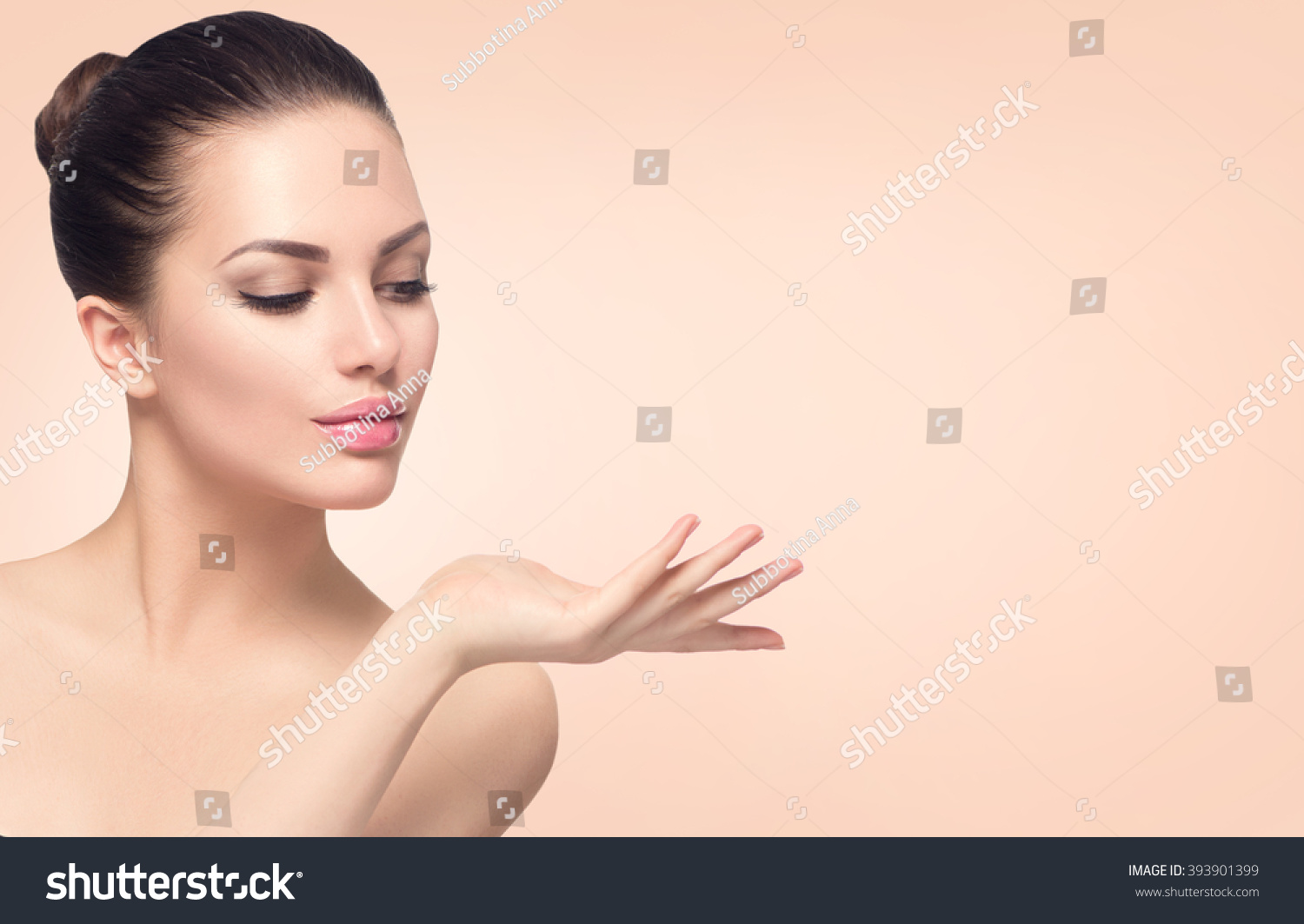 Beauty Spa Woman with perfect skin Portrait. Beautiful Brunette Spa Girl showing empty copy space on the open hand palm for text. Proposing a product. Gestures for advertisement. Beige background #393901399