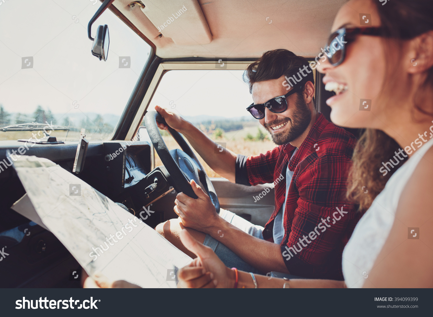Happy young couple with a map in the car. Smiling man and woman using map on roadtrip. #394099399