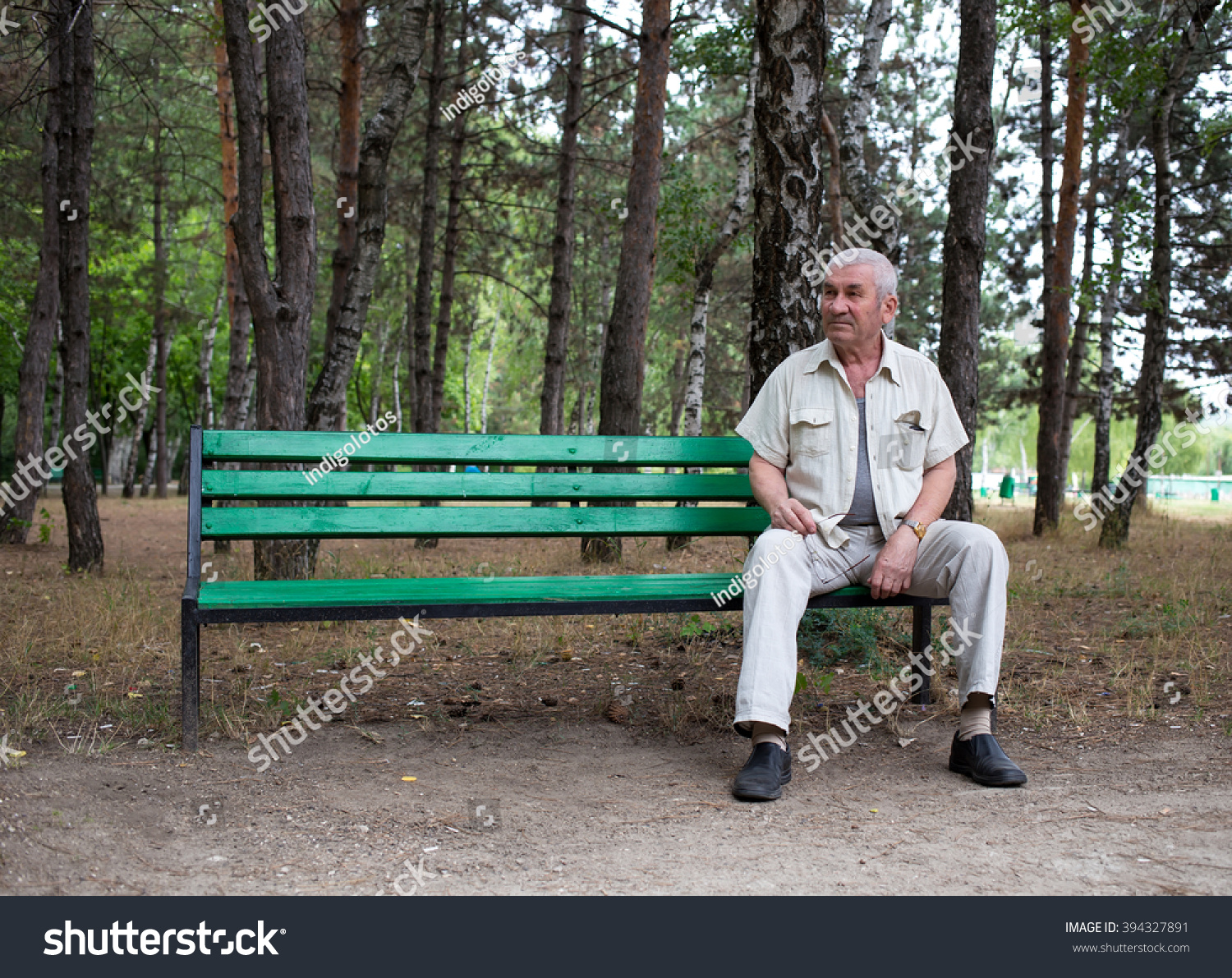 Old man sitting on the bench in park against trees as a background. #394327891