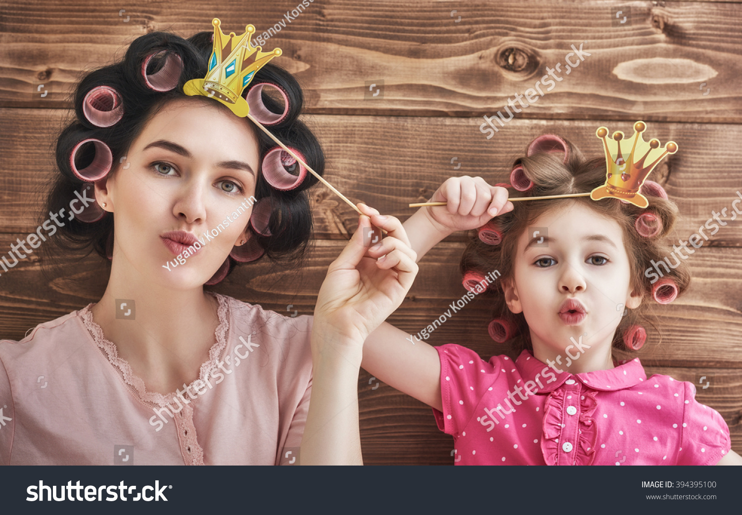 Funny family! Mother and her child daughter girl with a paper accessories. Beauty funny girl holding paper crown on stick. Beautiful young woman holding paper crown on stick. #394395100