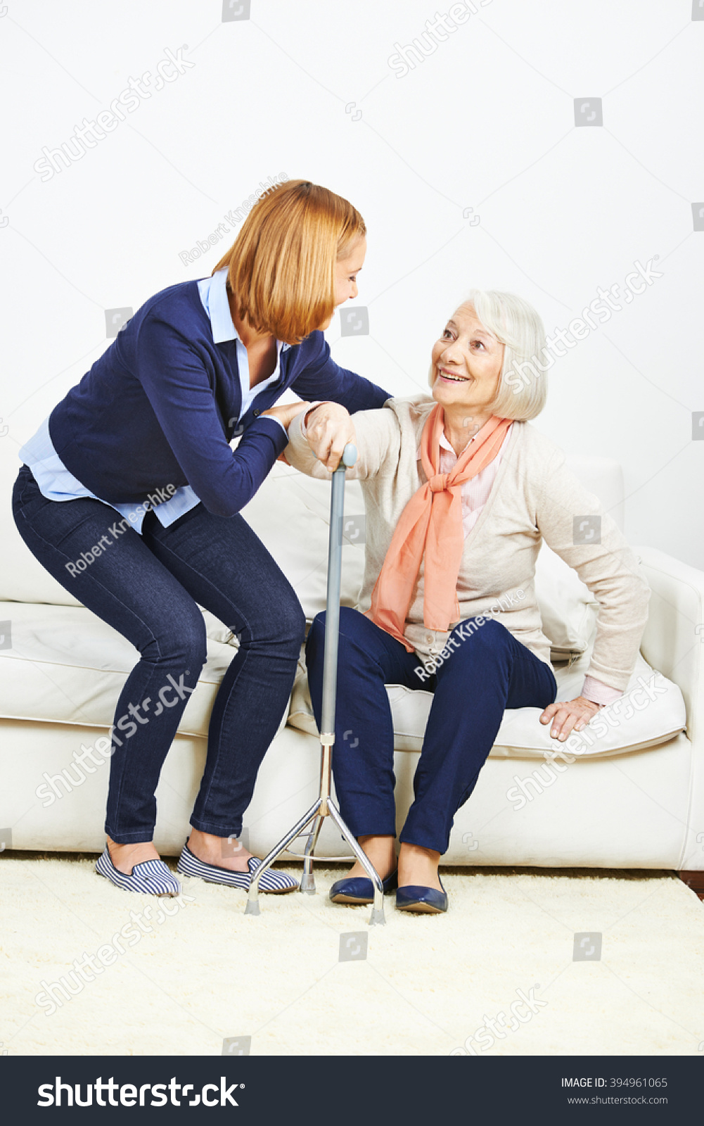 Woman helping senior woman with cane getting up from a sofa #394961065