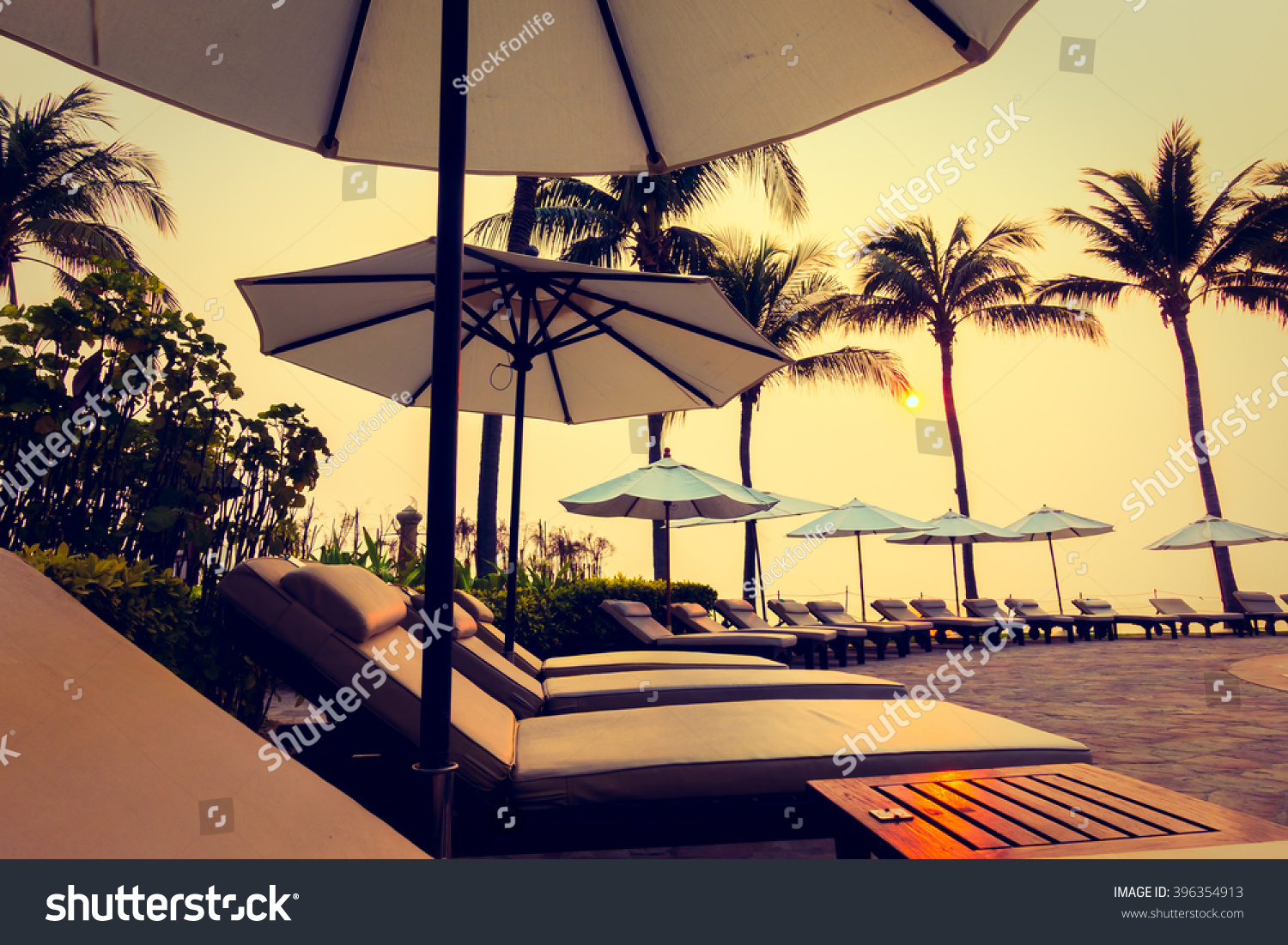 Beautiful Silhouette luxury umbrella and chair around swimming pool in hotel pool resort with coconut palm tree at sunrise times - Vintage Filter and Boost up color Processing #396354913