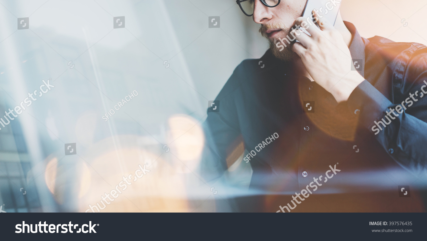 Photo bearded adult hipster working on modern urban cafe. Man wearing black shirt and speaking contemporary smartphone. Wide, film effect, bokeh. Blurred background #397576435