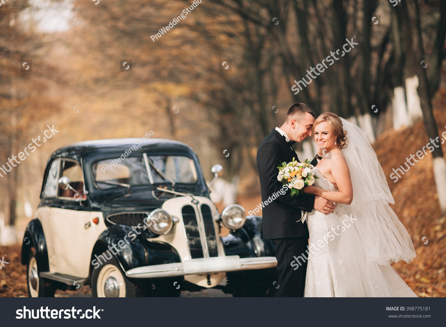 Stylish wedding couple, bride, groom kissing and hugging near retro car in autumn #398775181